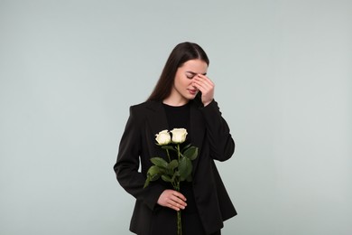 Sad woman with white rose flowers mourning on light grey background. Funeral ceremony