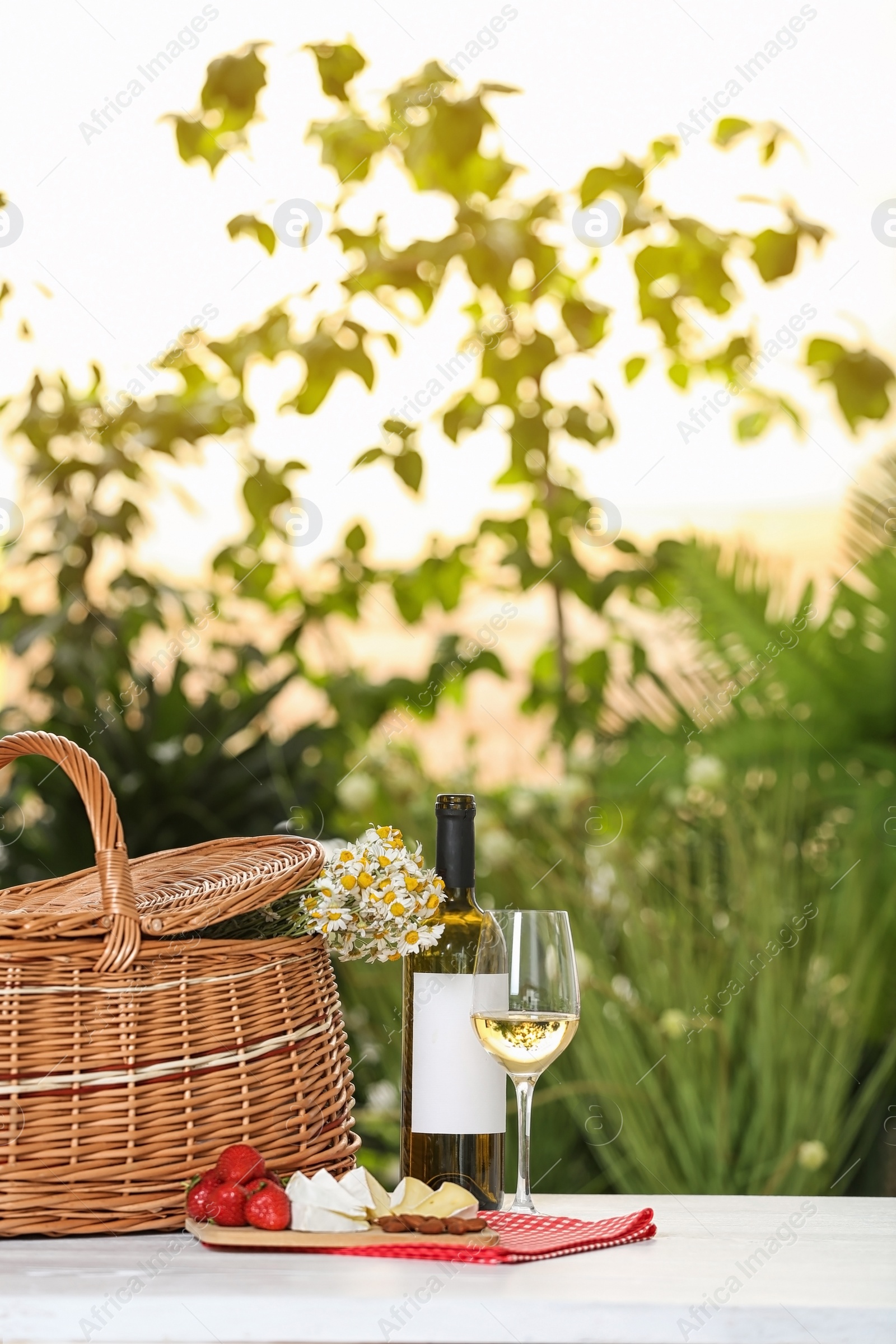 Photo of Picnic basket and wine with products on table against blurred background, space for text