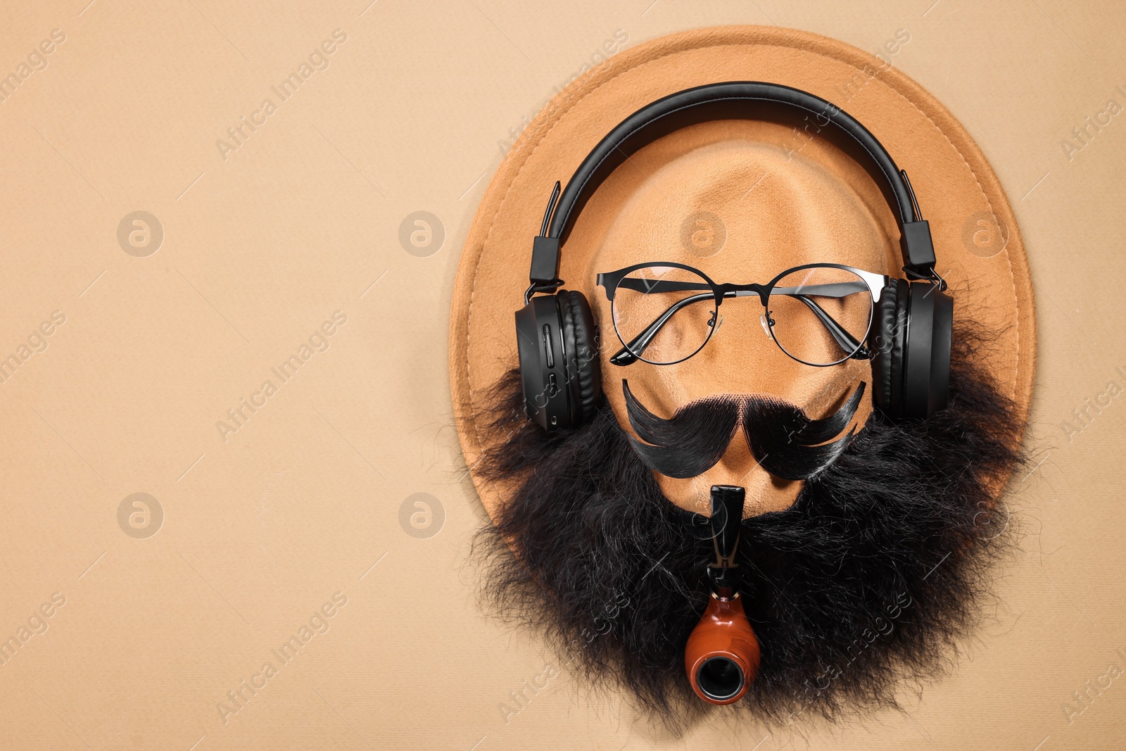 Photo of Man's face made of artificial mustache, beard, glasses and hat on beige background, top view. Space for text