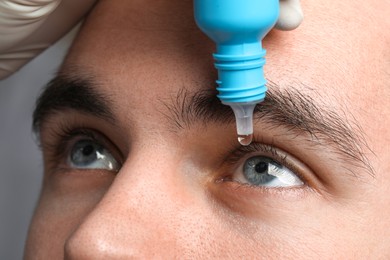 Doctor applying medical drops into young man's eye, macro view