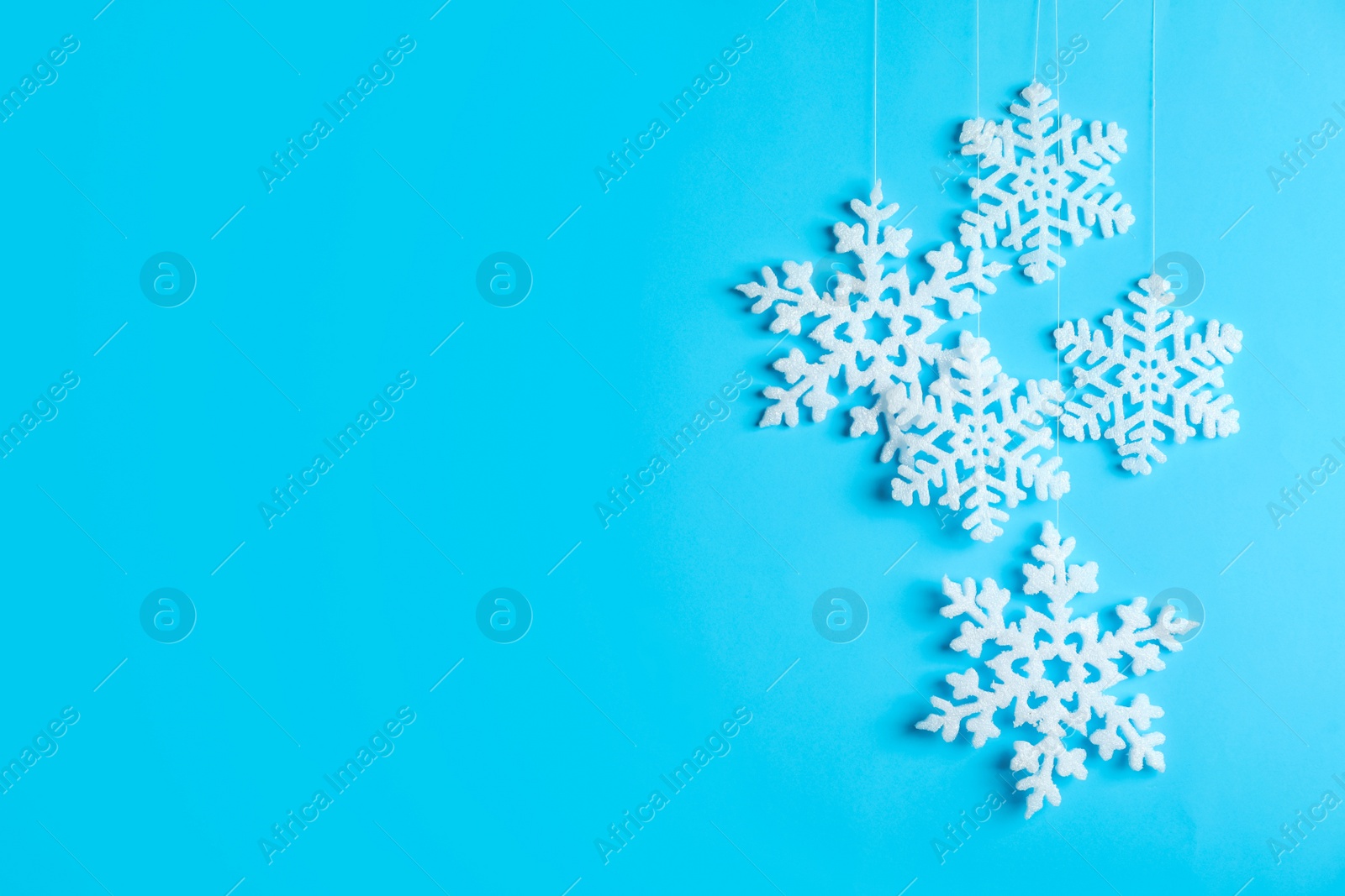 Photo of Beautiful decorative snowflakes hanging on light blue background, space for text