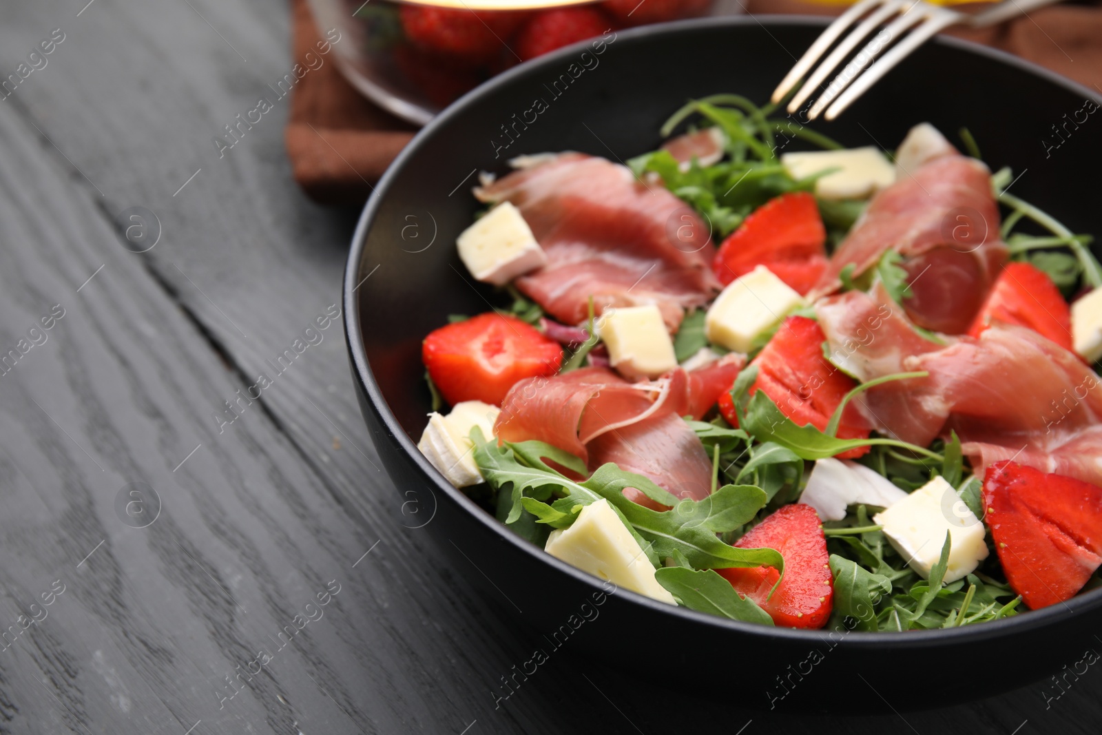 Photo of Tasty salad with brie cheese, prosciutto and strawberries on grey wooden table, closeup. Space for text