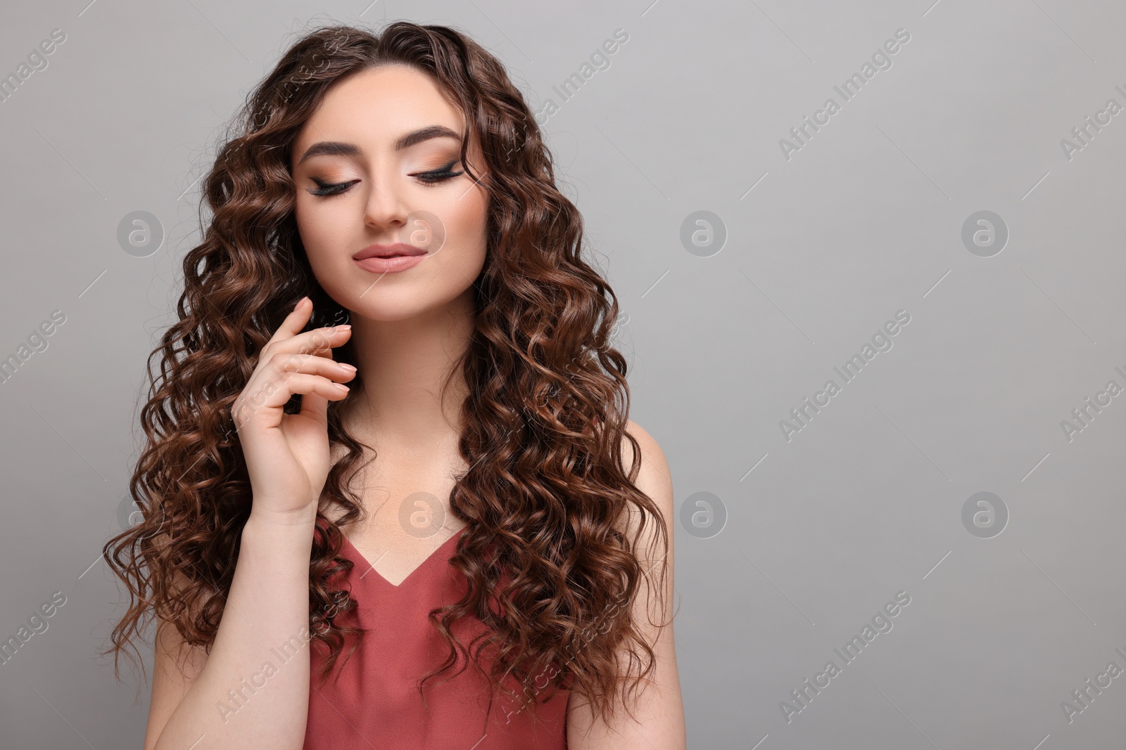 Photo of Beautiful young woman with long curly brown hair on grey background, space for text