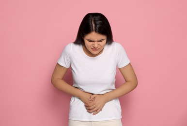 Photo of Young woman suffering from menstrual pain on pink background, space for text