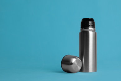 Stylish thermo bottle on light blue background, space for text