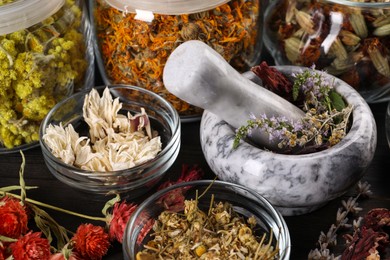 Photo of Mortar with pestle and many different herbs on table, closeup