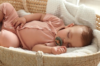 Photo of Cute little baby with pacifier sleeping in wicker crib at home