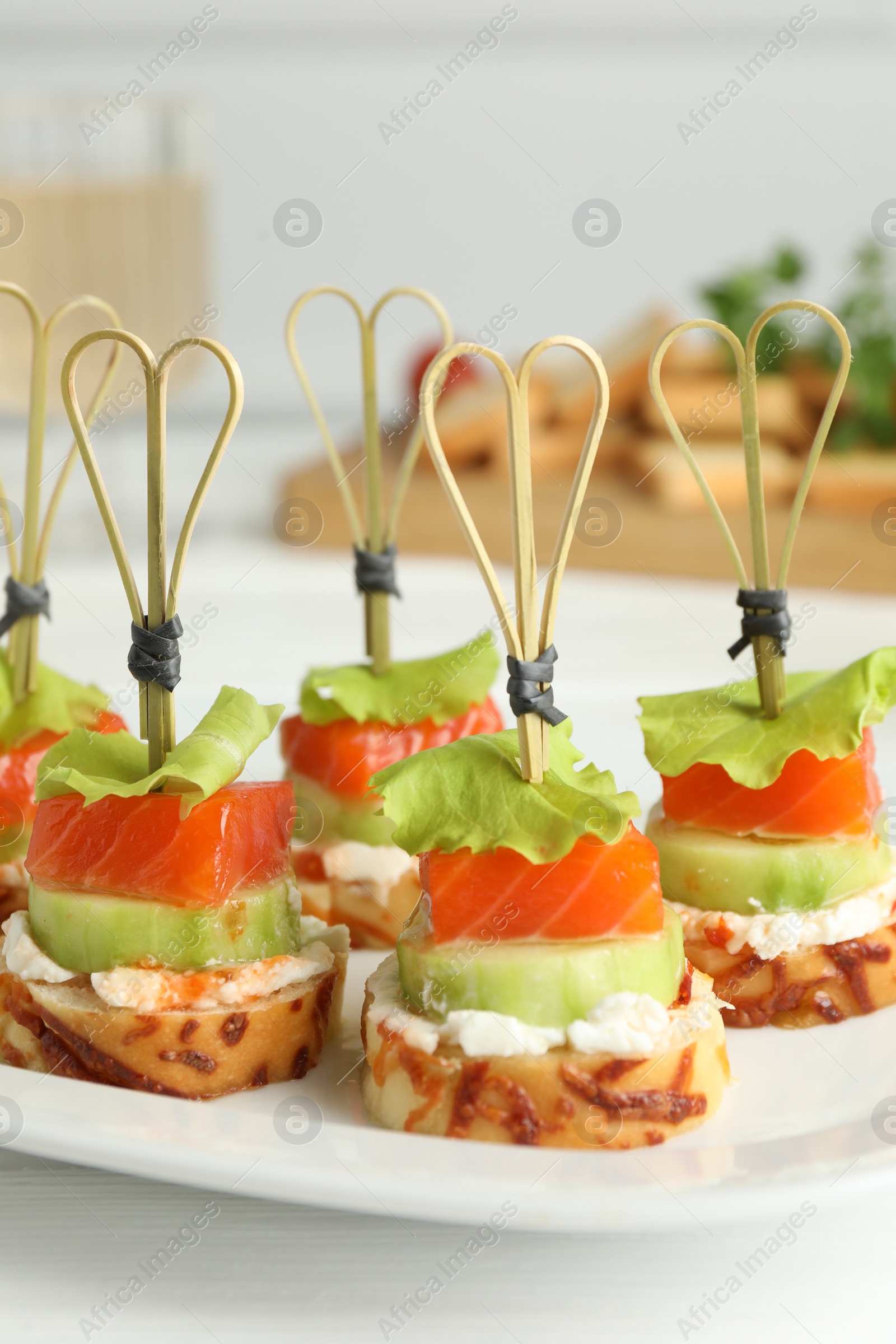 Photo of Tasty canapes with salmon, cucumber, bread and cream cheese on white table, closeup