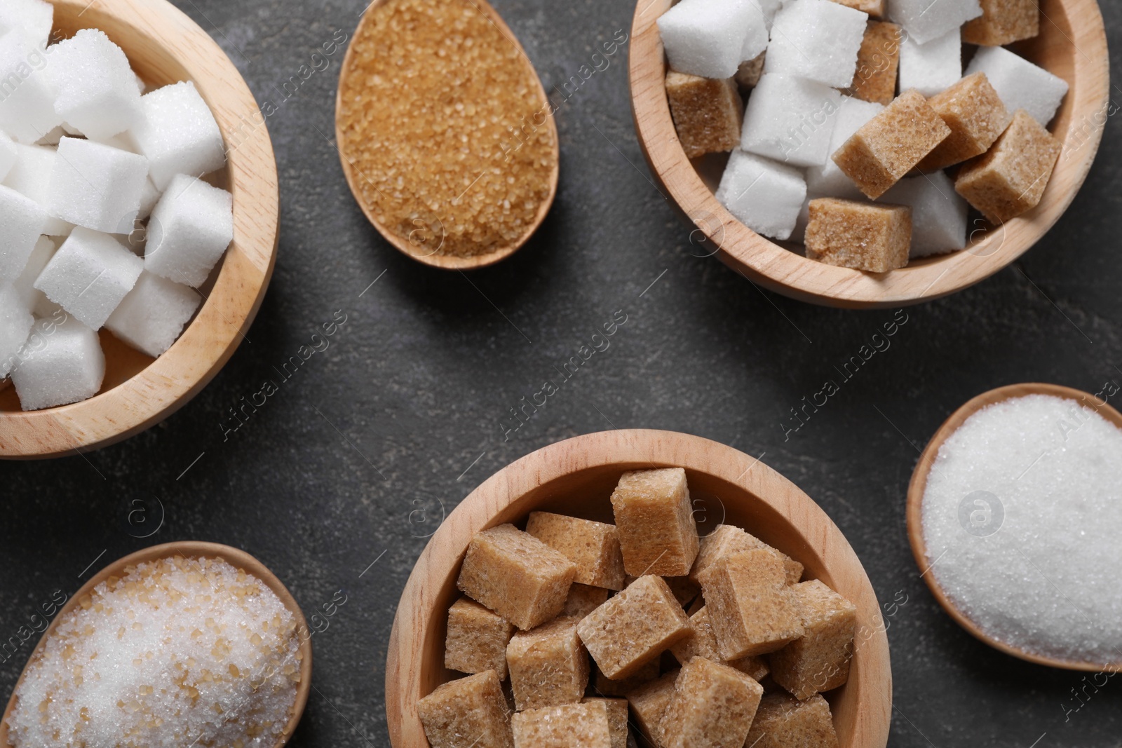 Photo of Bowls and spoons with different types of sugar on gray table, flat lay