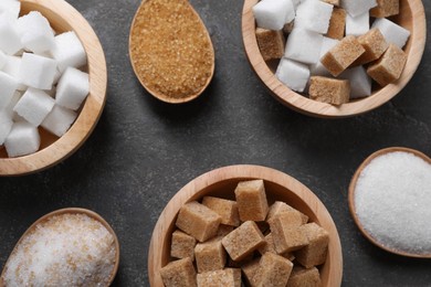 Bowls and spoons with different types of sugar on gray table, flat lay