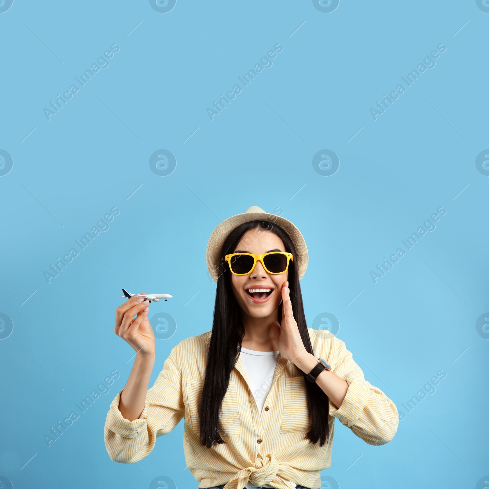 Photo of Happy female tourist with toy plane on light blue background