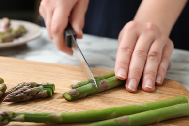 Photo of Woman cutting asparagus on wooden board, closeup
