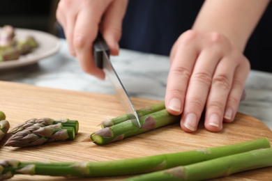 Woman cutting asparagus on wooden board, closeup