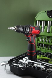 Photo of Electric screwdriver and case with drill bits on white table against pale green background