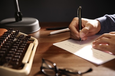 Photo of Man writing letter at wooden table indoors, closeup