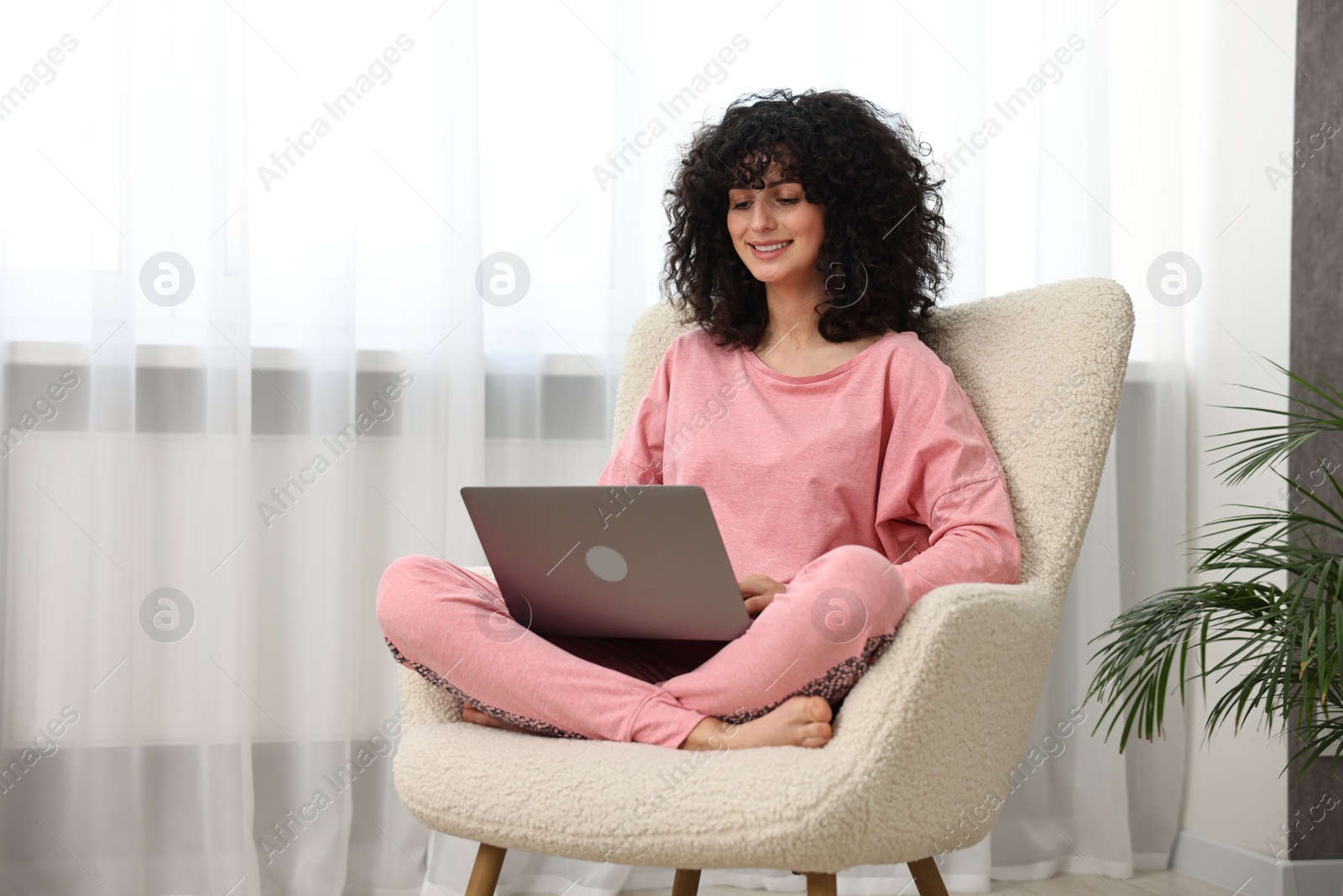 Photo of Beautiful young woman in stylish pyjama with laptop on armchair at home