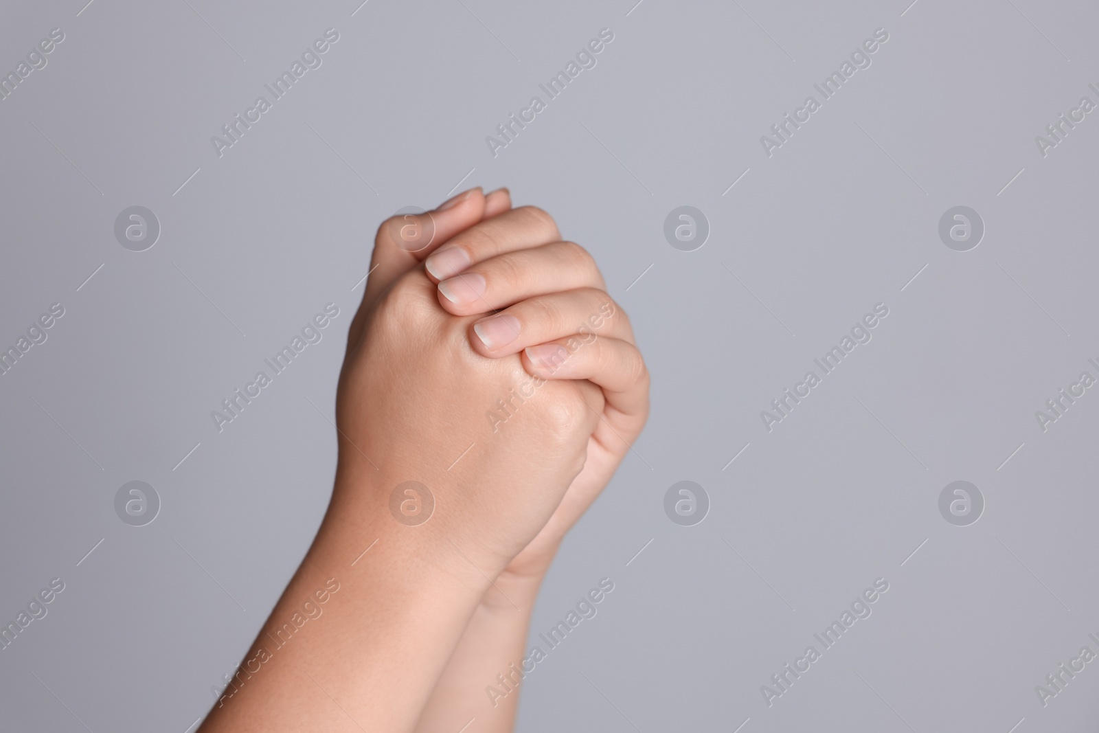 Photo of Woman holding hands clasped while praying against light grey background, closeup. Space for text