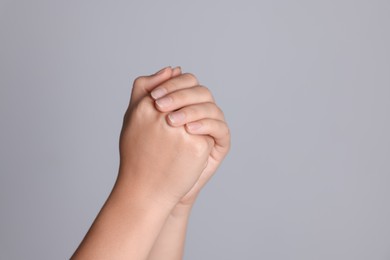 Woman holding hands clasped while praying against light grey background, closeup. Space for text