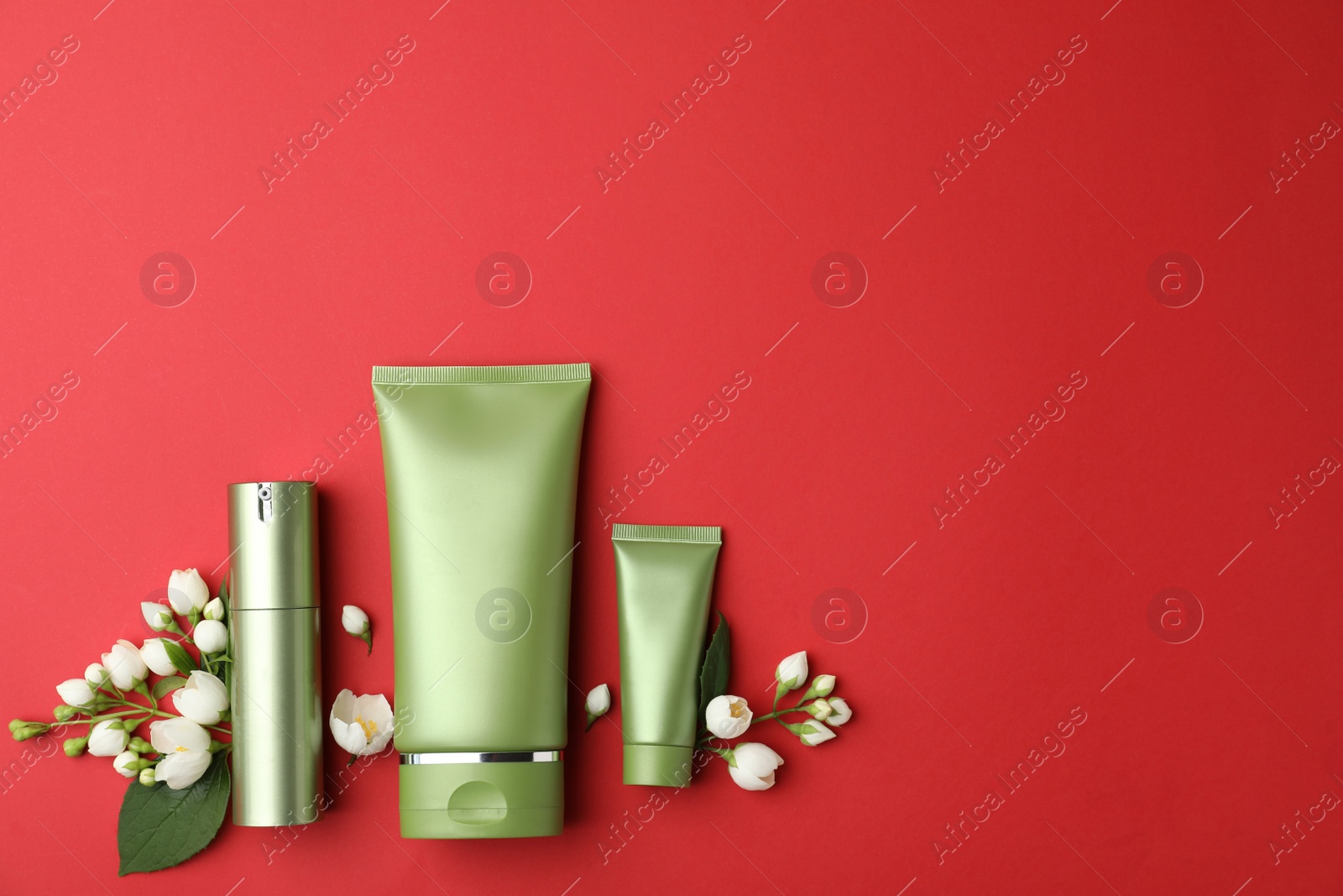 Photo of Set of cosmetic products and flowers on red background, flat lay. Space for text