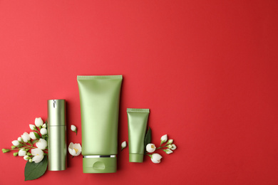 Set of cosmetic products and flowers on red background, flat lay. Space for text