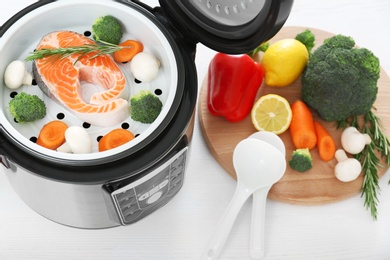 Modern multi cooker and products on white wooden table, above view