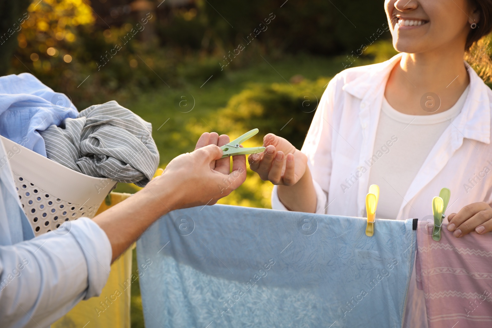 Photo of Happy family hanging clothes with clothespins on washing line for drying in backyard, closeup