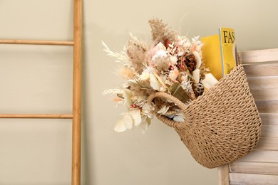 Stylish beach bag with beautiful bouquet of dried flowers and magazine hanging on folding screen indoors