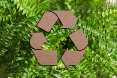 Image of Recycling symbol cut out of kraft paper and fresh green leaves on background