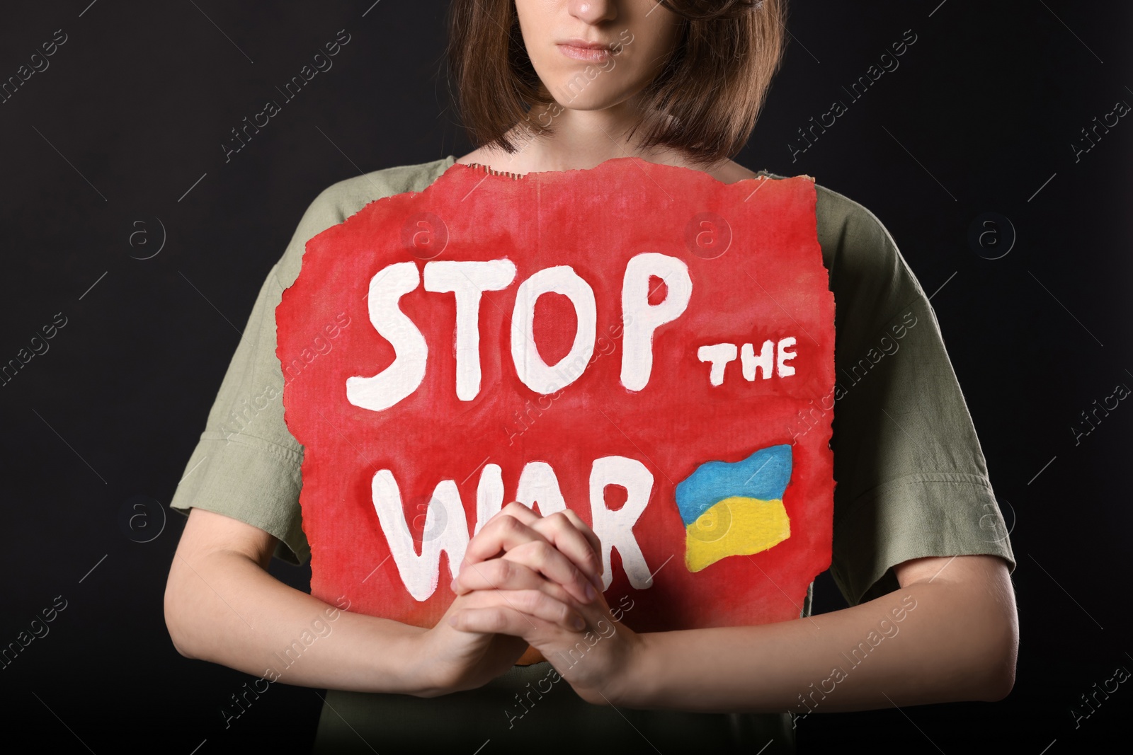 Photo of Sad woman holding poster with words Stop the War on black background, closeup