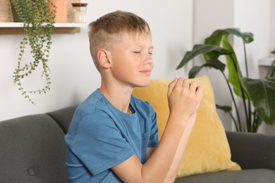 Photo of Boy with clasped hands praying on sofa at home