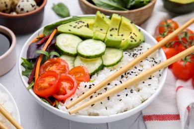 Delicious poke bowl with vegetables, avocado and mesclun on white table, closeup
