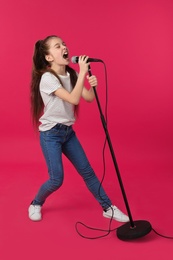 Cute girl singing in microphone on color background