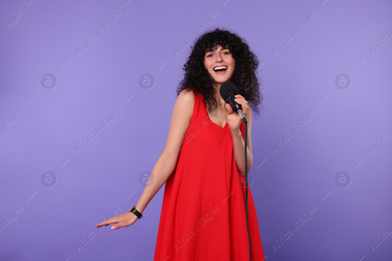 Photo of Beautiful young woman with microphone singing on purple background