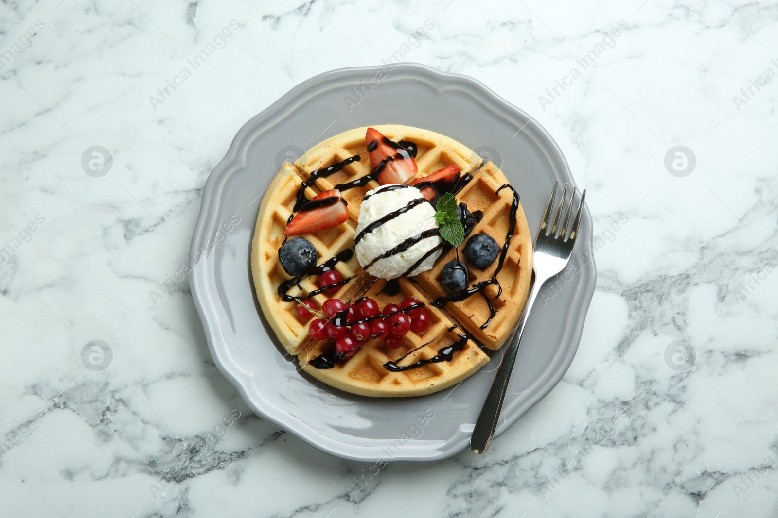 Photo of Delicious Belgian waffles with ice cream, berries and chocolate sauce on light marble table, top view