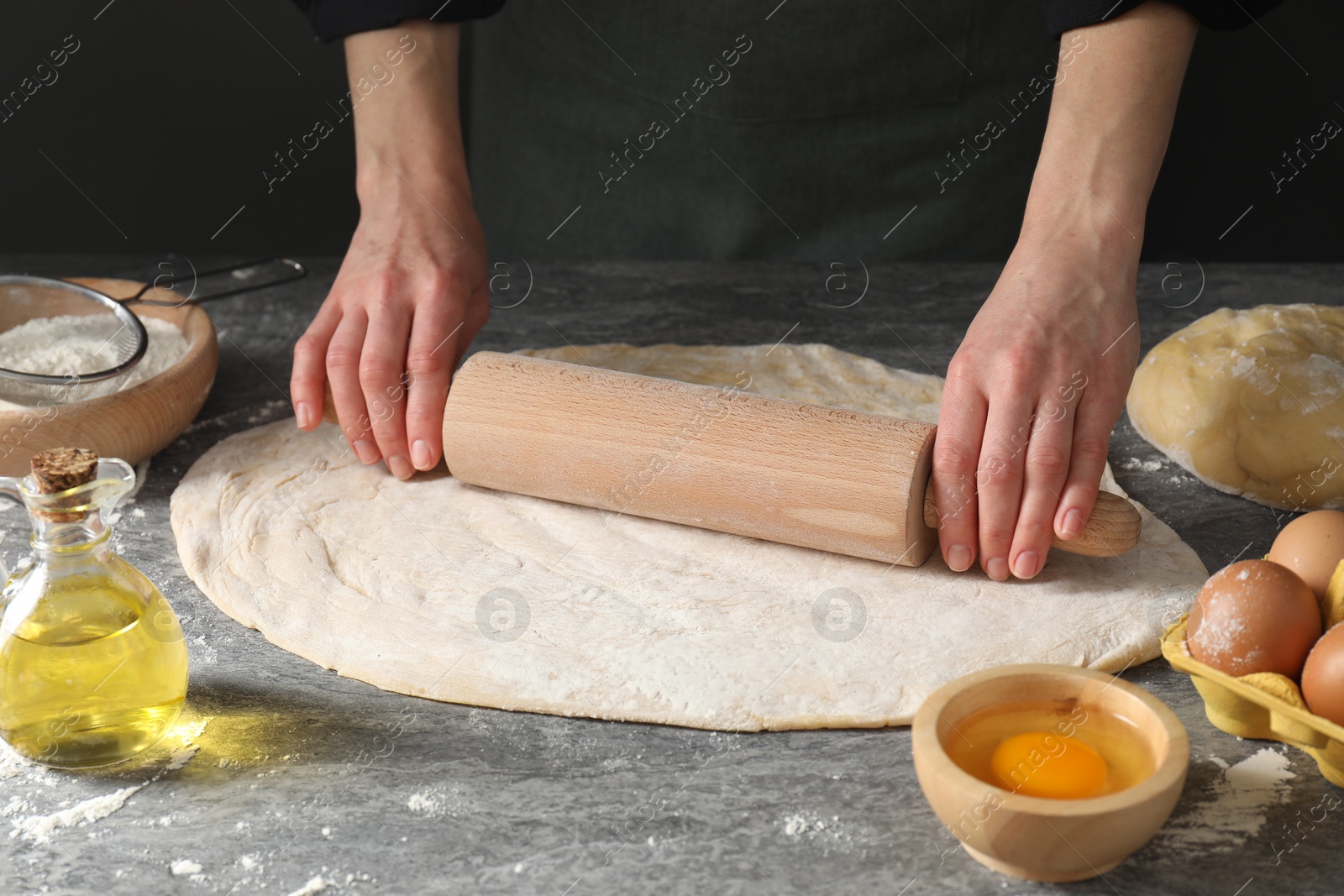 Photo of Woman rolling raw dough at grey table, closeup