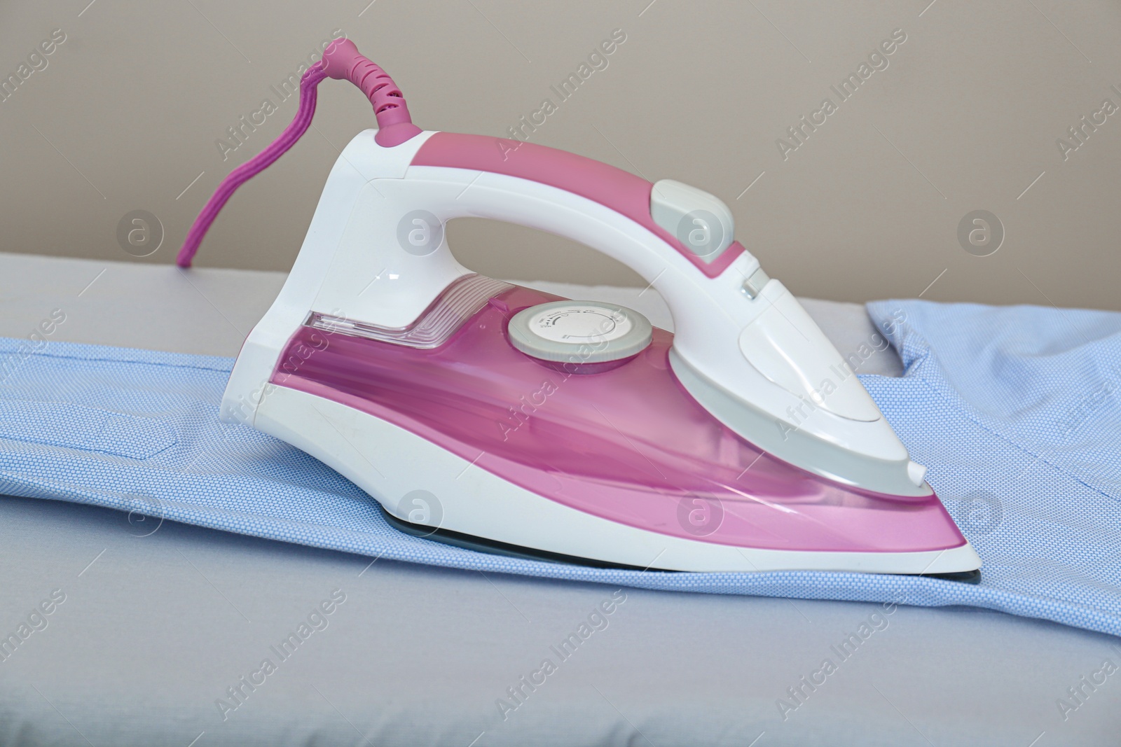 Photo of Modern iron and clean shirt on board indoors against beige background