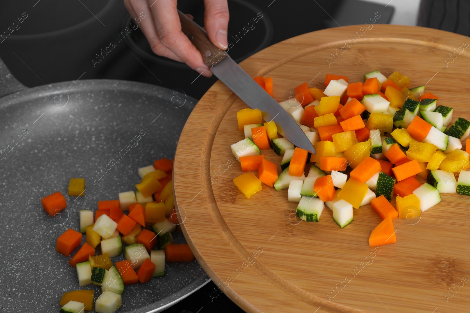 Photo of Woman putting cut vegetables onto frying pan in kitchen, closeup