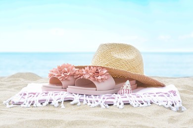 Blanket with slippers, straw hat and seashell on sand near sea. Beach accessories