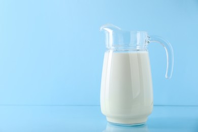 Jug of fresh milk on light blue background, space for text