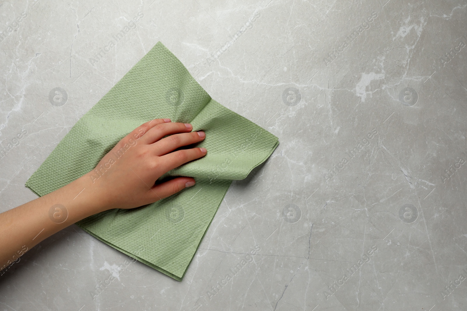 Photo of Woman cleaning light grey table with paper towel, top view. Space for text