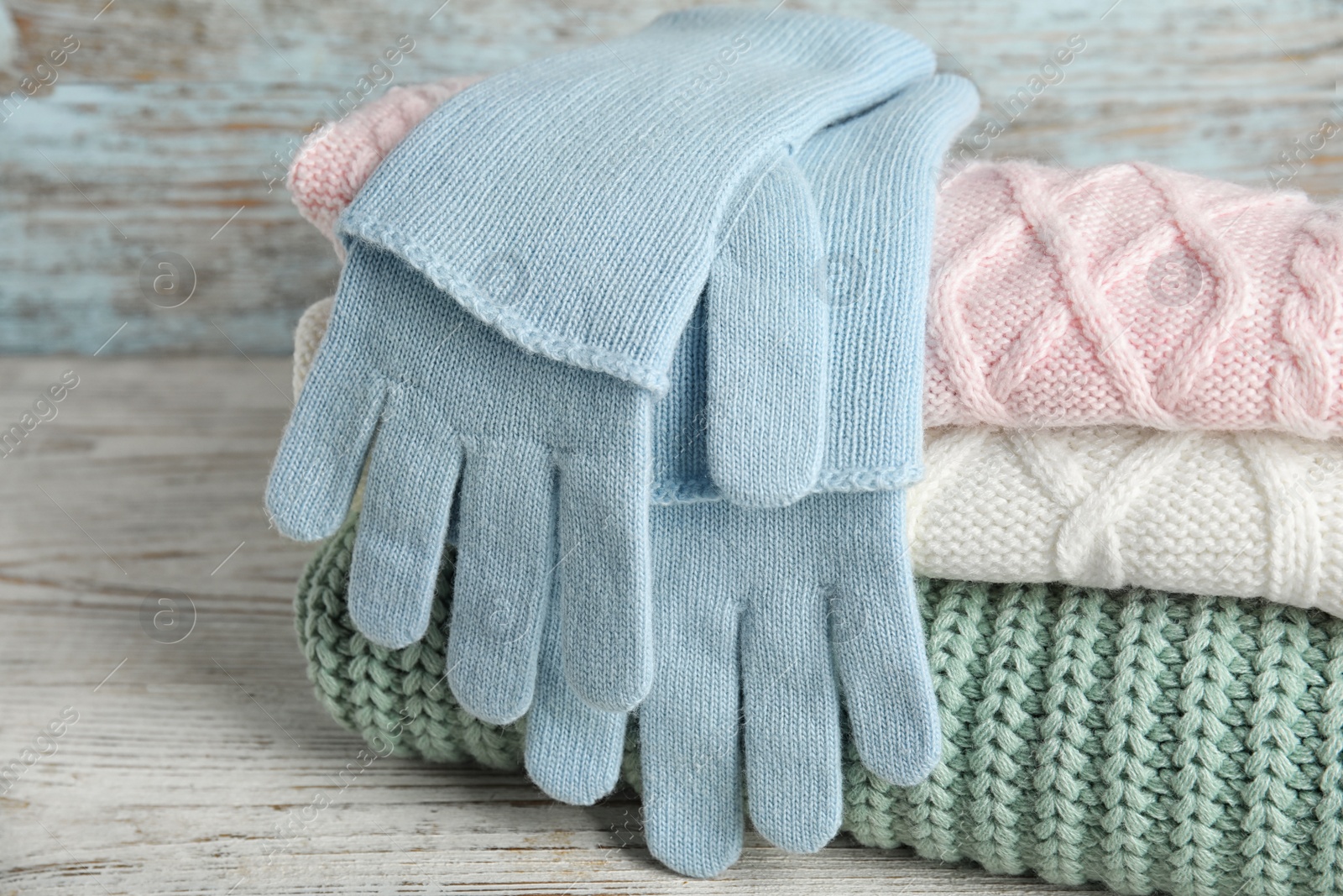 Photo of Stacked sweaters and gloves on wooden table, closeup. Autumn clothes