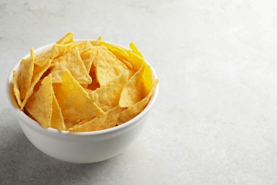 Photo of Bowl with tasty tortilla chips (nachos) on grey table. Space for text