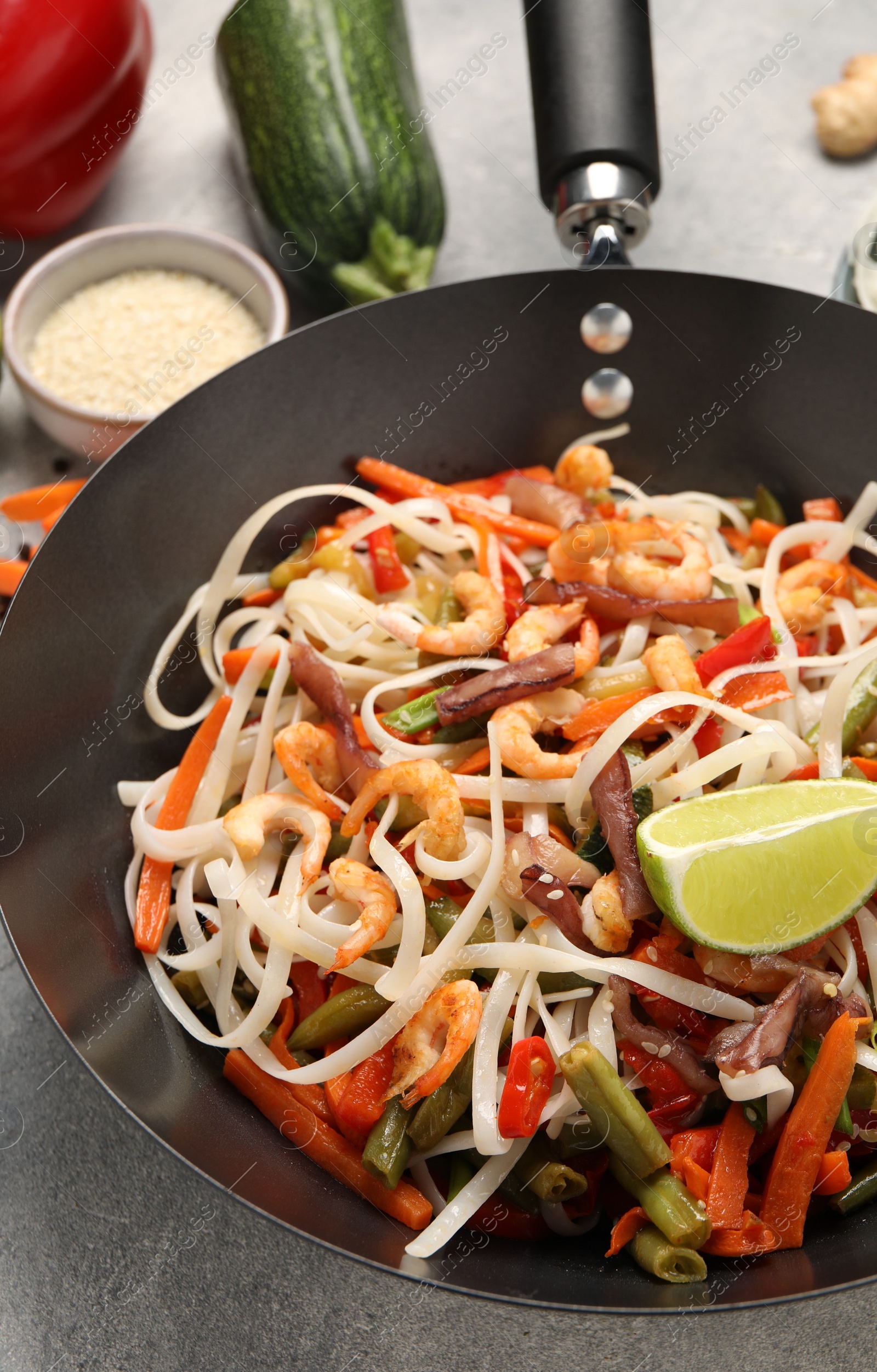 Photo of Shrimp stir fry with noodles and vegetables in wok on grey table, closeup