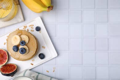Photo of Tasty oatmeal pancakes on white tiled table, flat lay. Space for text