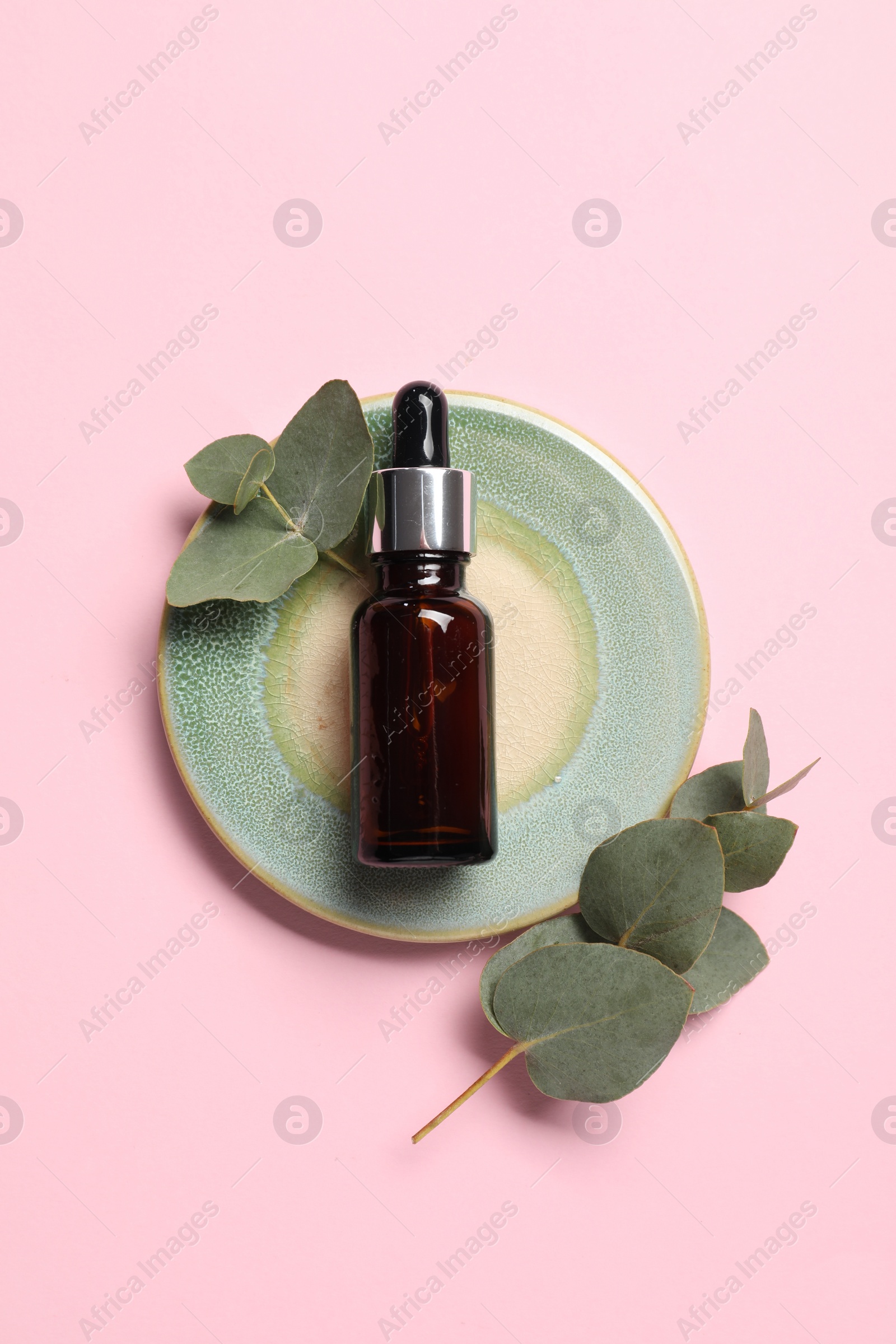 Photo of Aromatherapy product. Bottle of essential oil and eucalyptus leaves on pink background, top view