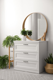 Photo of Round mirror and chest of drawers near white wall in room. Modern interior design