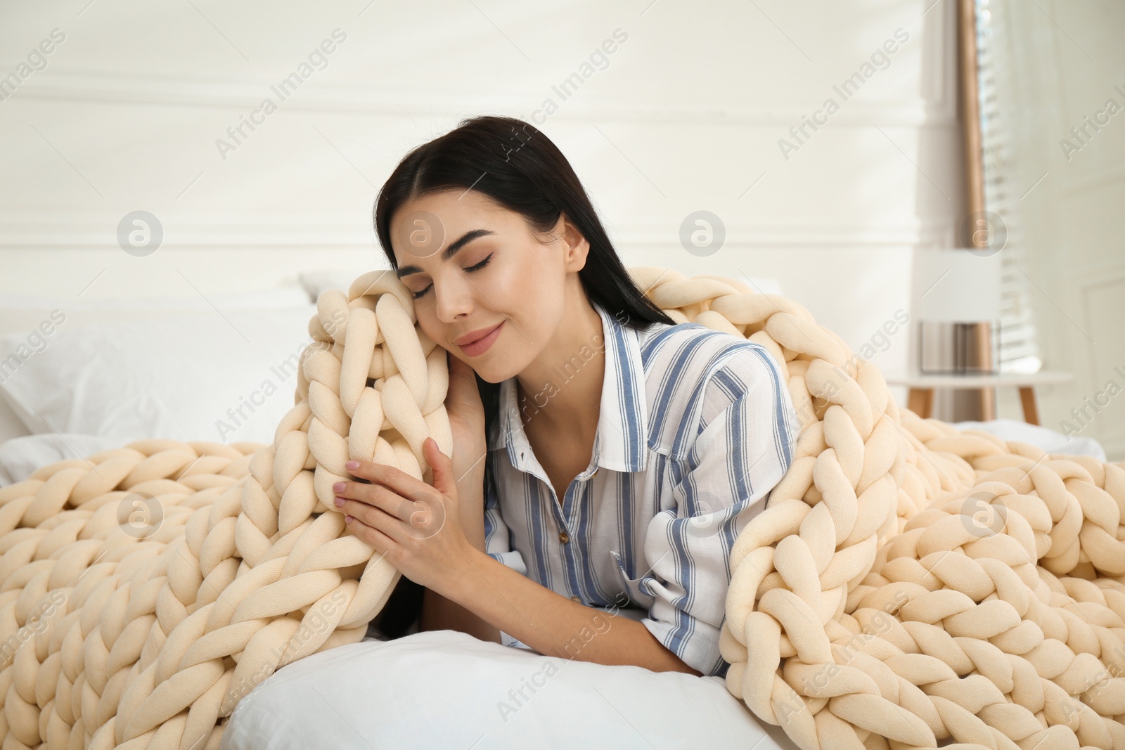 Photo of Young woman with chunky knit blanket on bed at home