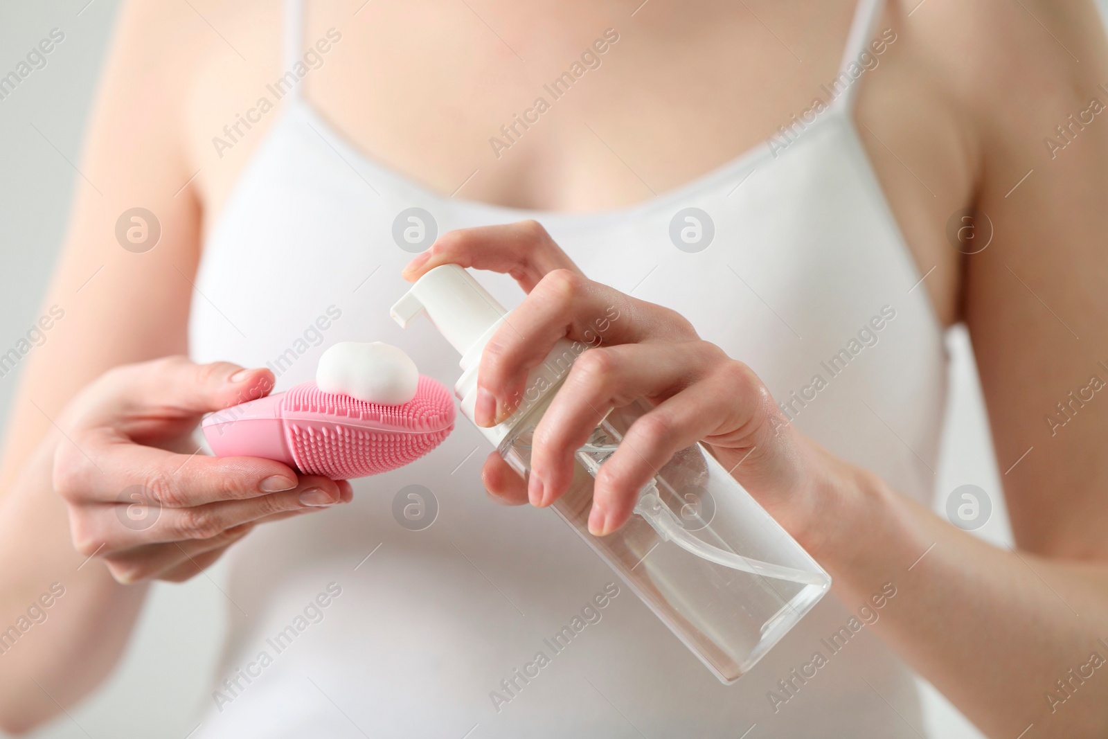 Photo of Washing face. Woman applying cleansing foam onto brush against light background, closeup