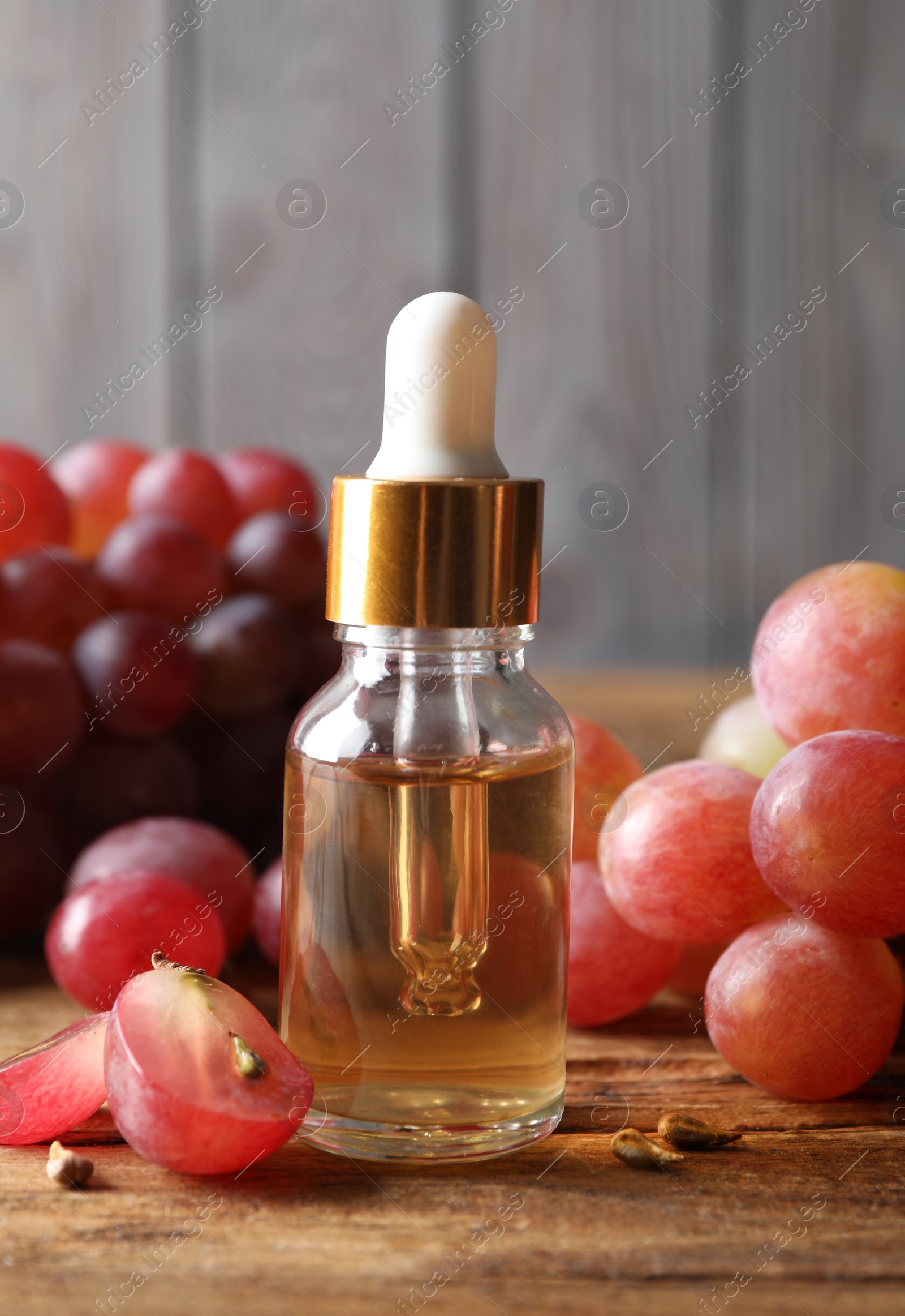 Photo of Organic red grapes, seeds and bottle of natural essential oil on wooden table