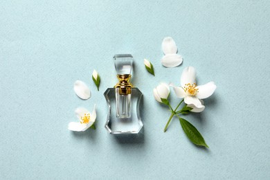 Photo of Bottle of luxury perfume and fresh jasmine flowers on light blue background, flat lay